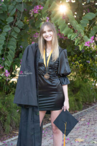 ucf graduate in her cap and gown standing by a bush of flowers