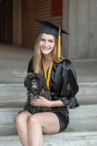 ucf graduate is sitting on stairs holding her little black dog