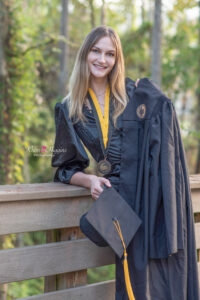 ucf graduate is holding her cap and gown and leaning on a boardwalk behind student union