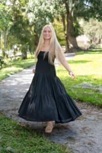 A blond Hagerty High School senior girl in a black sundress is twirling by a lake.