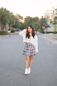 orlando senior girl in a white sweater with checkered short skirt is walking in the middle of a road.