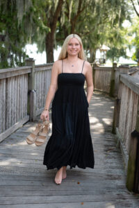 A blond Hagerty High School senior girl in a black sundress is walking on a boardwalk by a lake.