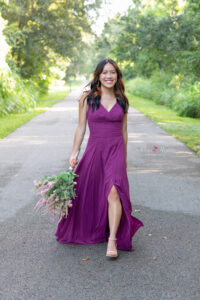 Orlando senior girl in a purple prom dress is holding flowers and walking on a side street.