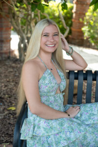 A Hagerty senior girl in a blue dress is sitting on a black metal bench at Park Ave. in Winter park.