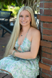 A Hagerty senior girl in a blue dress is leaning against a brick pillar.