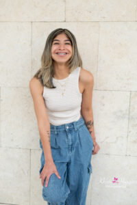 senior girl wearing a cream color sleevelsss tank with blue jeans is leaning on a white wall.