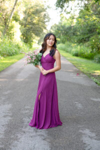 orlando senior girl in a purple color formal dress is holding flowers standing on a side road.