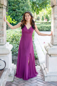 orlando senior girl in a purple color formal dress is standing between two brick pillars with each hand touching the pillar.