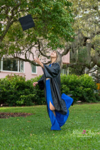 senior girl wearing her black graduation gown is tossing up her cap.