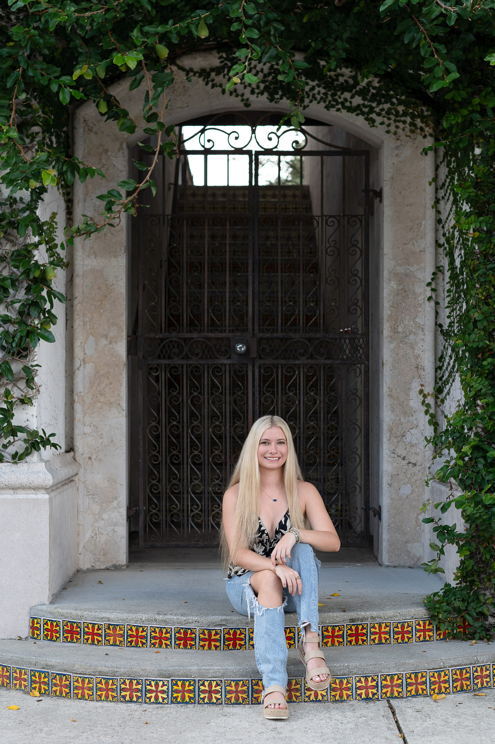 A blond Hagerty High School senior girl wearing jeans and a black and white top is sitting on a set of stairs.