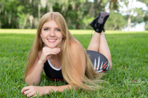 Oviedo high school senior girl is wearing her wrestling singlet is laying on the grass with her hand under her chin.