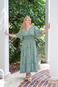 Oviedo high school senior girl is wearing a long green dress standing between two white pillars with her hands touching each pillar.