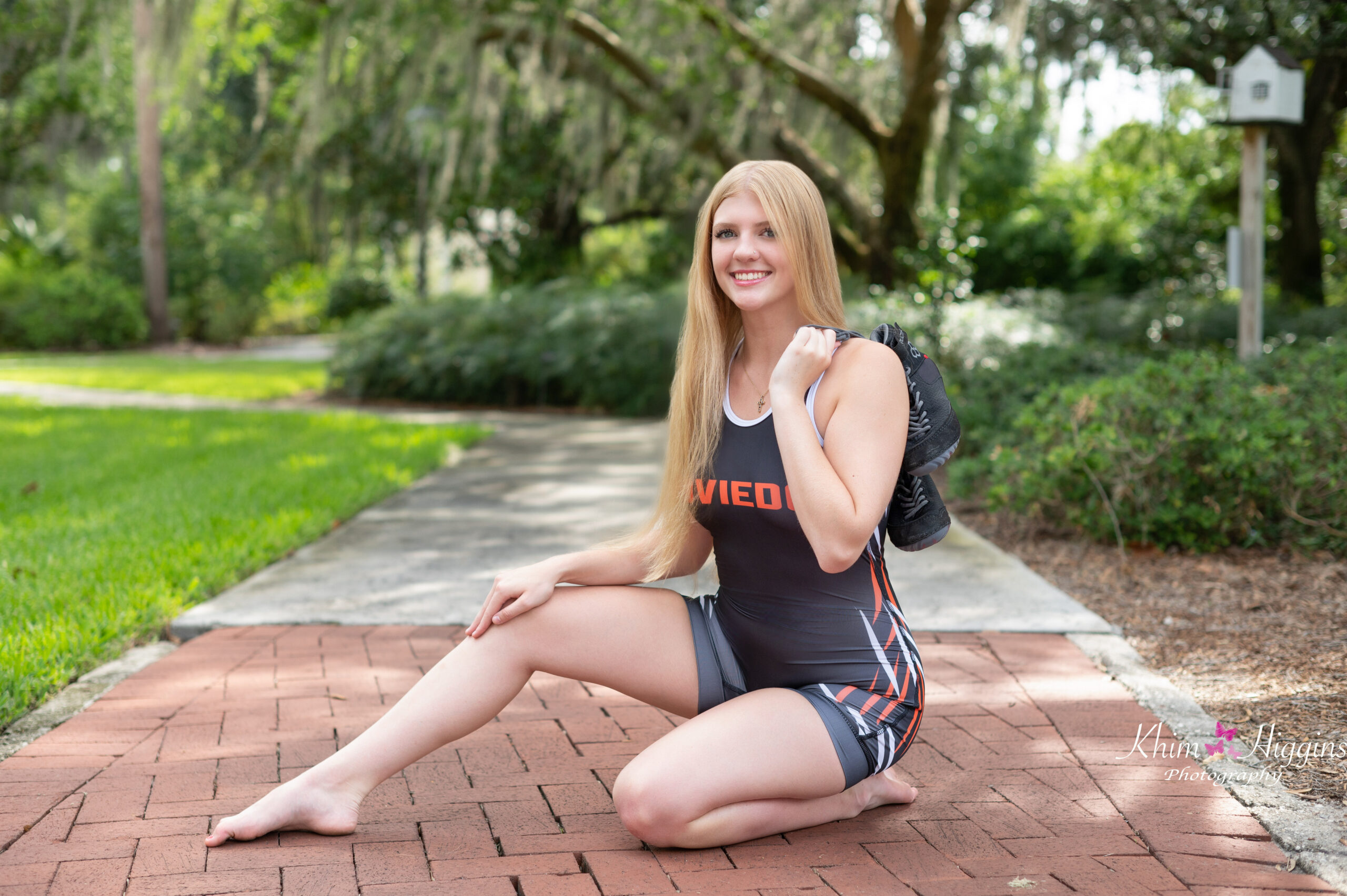 Oviedo high school senior girl is wearing her wrestling singlet and is sitting on the sidewalk.