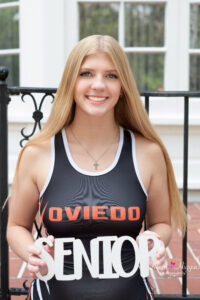 Oviedo high school senior girl is wearing her wrestling singlet and holding a 'senior' sign.