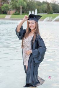 A senior girl wearing her cap and gown is standing in the Reflection Pond at UCF.