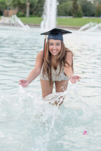 A senior girl in a white romper is splashing water at UCF Reflecting Pond.