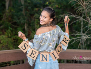 A senior girl holding a SENIOR banner is looking over her shoulder.