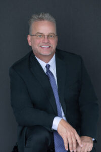 A white male in a black suit is sitting for his headshot photo with khim higgins photography.