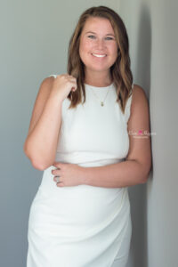 a woman wearing a white dress is leaning against a gray wall for her professional modern headshot with khim higgins photography.