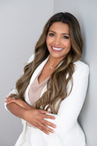 A beautiful brunette woman in a white suit jacket is leaning against a gray wall for a headshot with khim higgins photography in oviedo, florida.