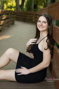 oviedo high school senior girl in a black dress is sitting at a dock at lake mills working with khim higgins photography.