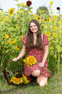 orlando senior girl holding sunflowers standing in front of a field of sunflowers while khim higgins photography takes her photo.