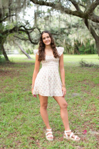 Oviedo high school senior girl standing in a field and she is wearing a short floral dress.