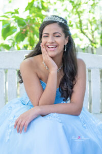 Sweet 16 girl in a blue formal dress is sittin on a bench smiling at Khim Higgins Photography.