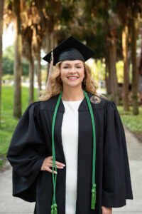 ucf graduate in cap and gown by the palm trees smiling