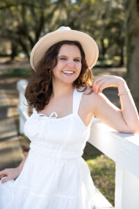 senior girl in white dress leaning on a fence in Oviedo, Fl
