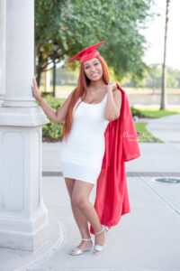 Senior girl in cap and gown leaning on pillar.