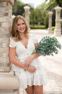 Oviedo senior girl holding flowers leaning on a pillar with Orlando senior photographer.