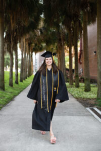 Senior girl in cap and gown walking near the palm trees