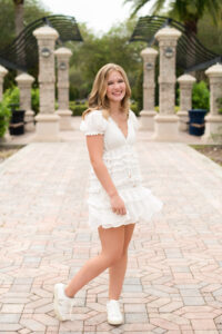 Oviedo senior girl in a white dress sways back and forth while Khim Higgins Photography takes her photos.