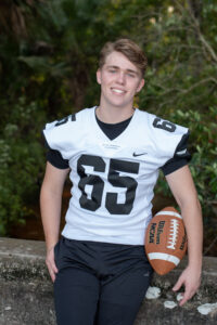 senior boy in football uniform holding a football during his orlando senior photo shoot