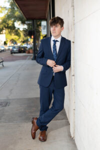 A winter park senior boy leans on a wall wearing a suit.