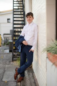 A senior boy in a suit leans on a wall.