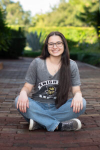 Girl in college t shirt sits on the ground for senior photos.