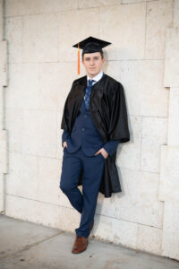 High school senior boy in a navy suit leaning on a wall at Rollins College in Winter Park