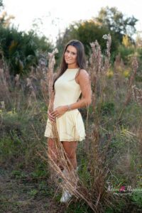 Senior girl smiling in an open field with warm sunset light.