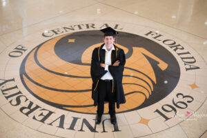 UCF graduate standing on the UCF seal during a graduation photo session.