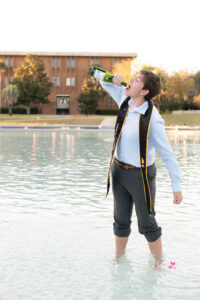 Graduate in cap and gown posing near the UCF Reflecting Pond at golden hour.
