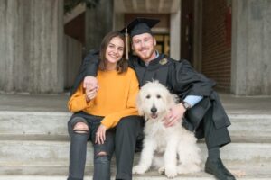 UCF graduate posing with his girlfriend and dog during a graduation photo session on campus.