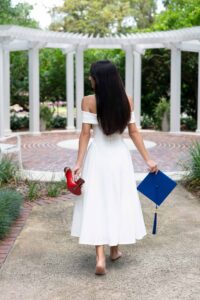 Senior girl holding her favorite shoes and graduation cap walking away.