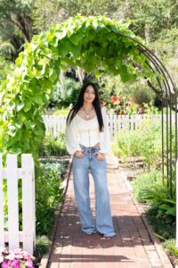 Orlando senior girl in jeans and a blowy cream colored top standing under an archway at Leu Gardens.