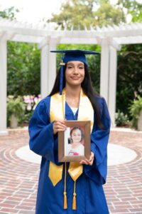 Orlando senior girl in her graduation cap and gown holding a baby photo.